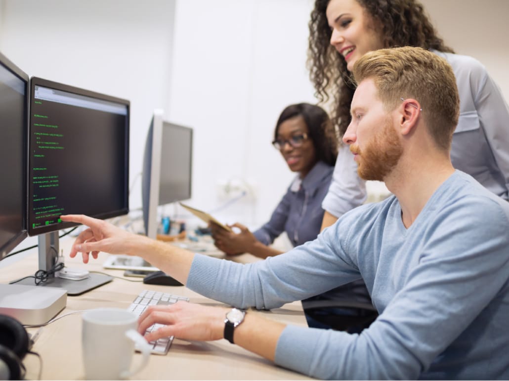 A team of professionals collaborating at a desk while reviewing code on dual monitors during an AWS migration project.
