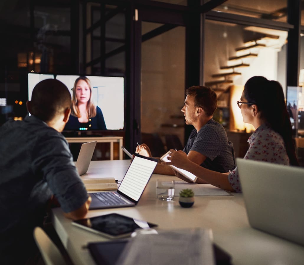 Team participating in a virtual meeting, watching a speaker on a screen in a modern office setting.