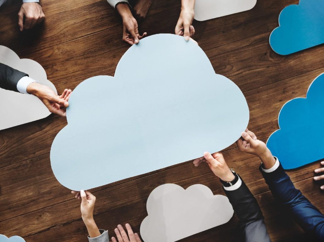 Multiple hands holding cutouts of cloud icons over a wooden table.
