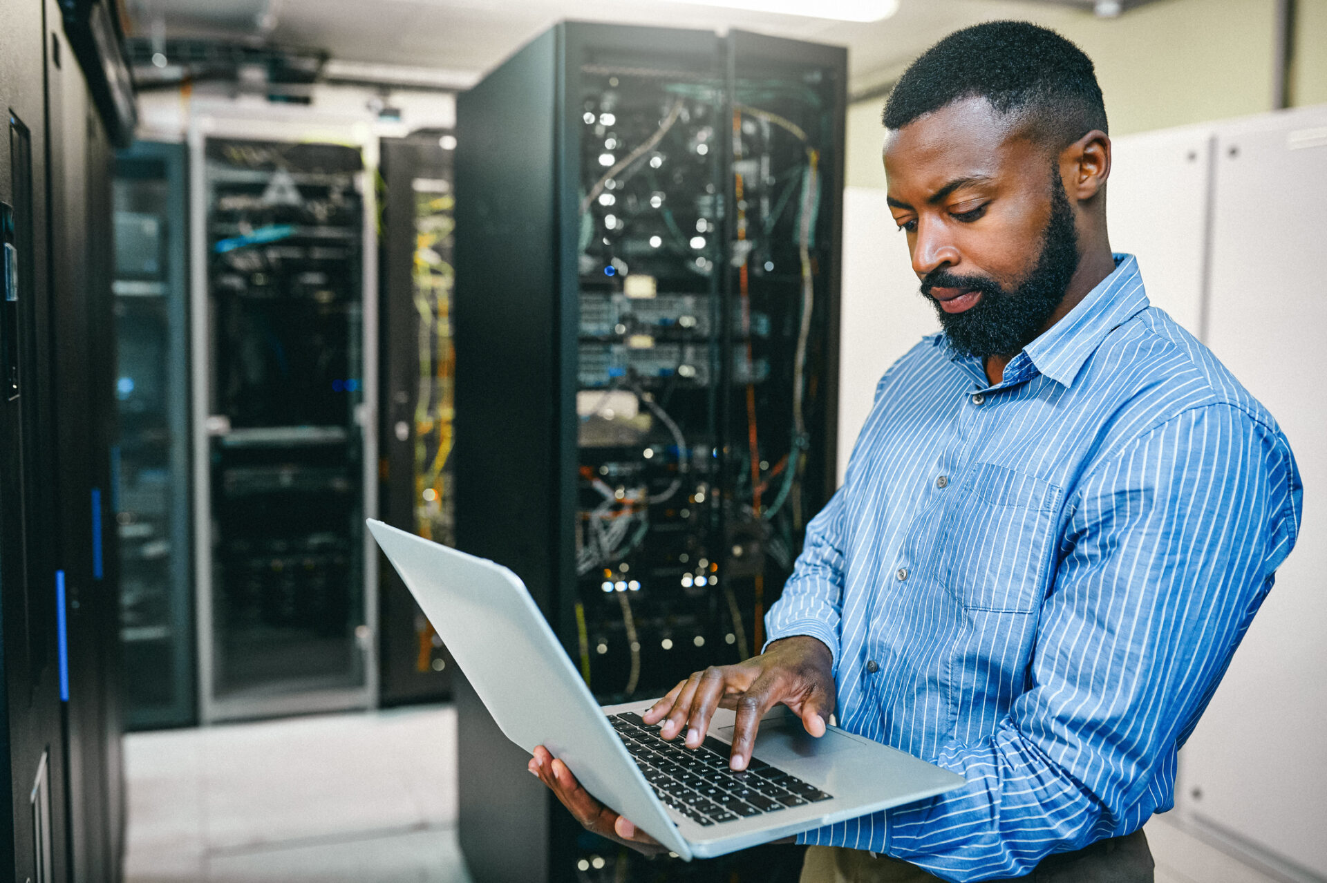 IT professional working on laptop in server room for AWS disaster recovery.