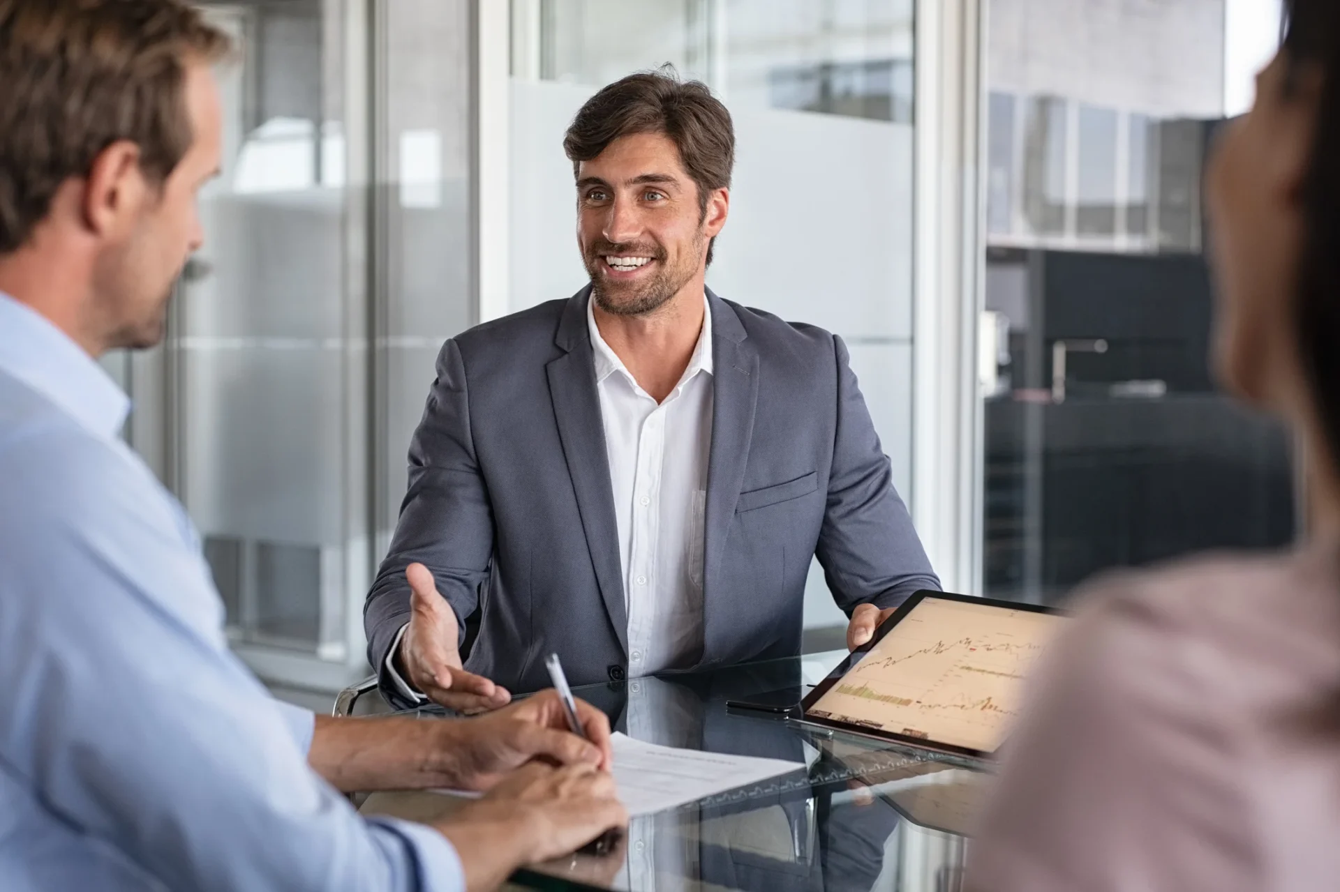 Business professional in a suit presenting charts on a tablet to two colleagues in a modern office, illustrating TekStream Expertise as a Service (EaaS) offering.
