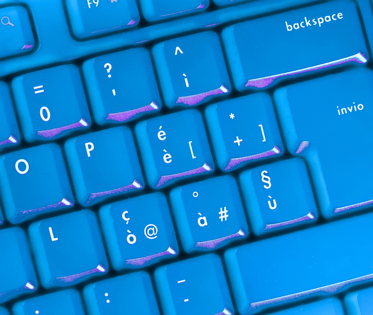 Close-up of a brightly colored blue keyboard with Italian or multilingual key symbols.