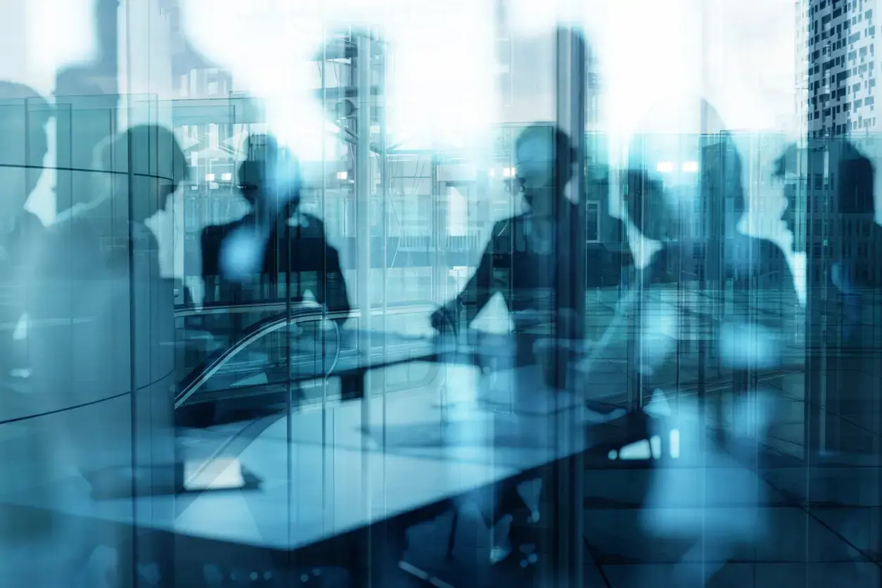 Silhouetted professionals in a glass-walled conference room collaborating around a table.