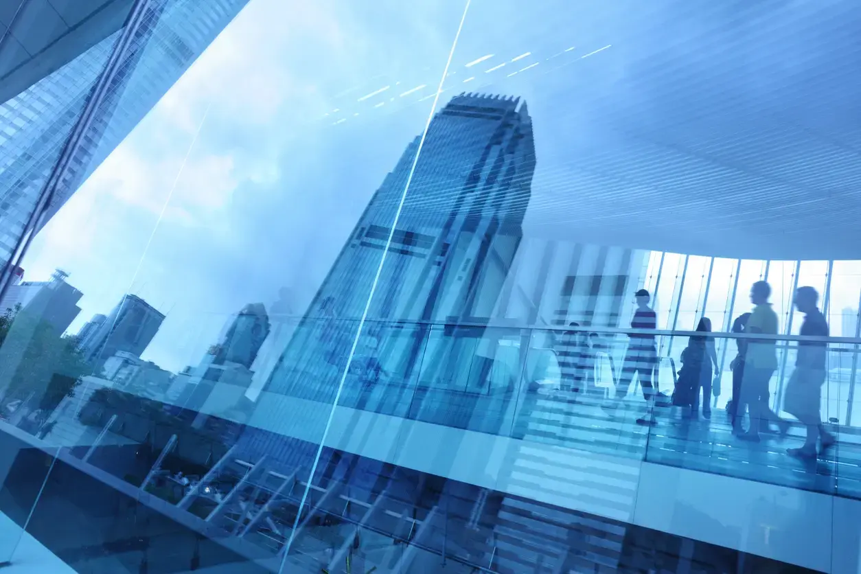 Business professionals walking inside a modern glass building with a city skyline reflected in the windows.