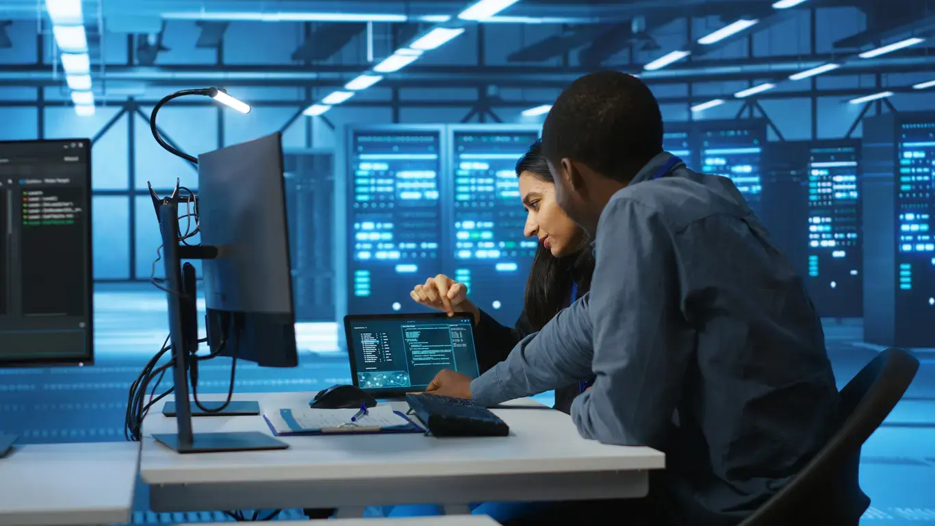 Two IT professionals in a data center reviewing security dashboards as part of a vulnerability assessment.
