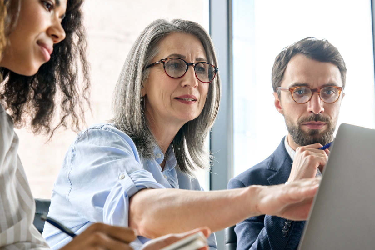 Diverse business professionals discussing strategy and reviewing data on a laptop during a meeting.