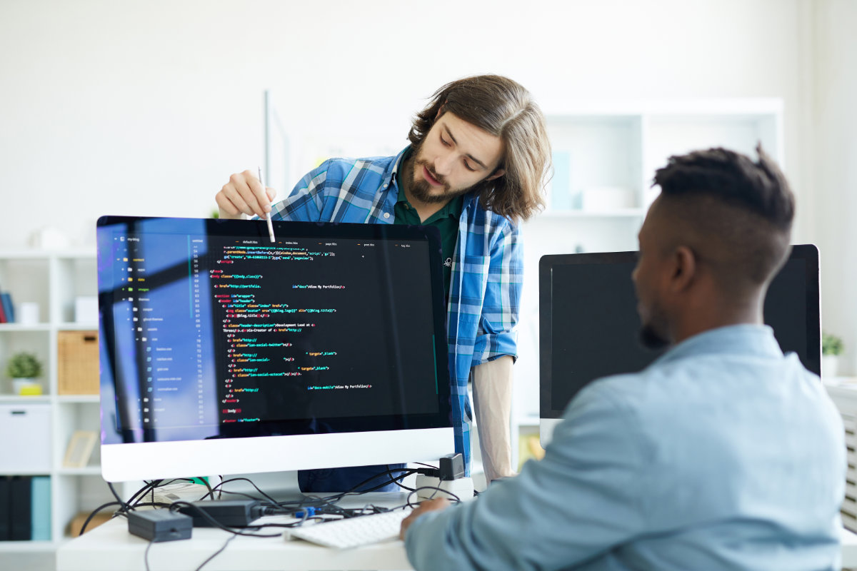 Two developers reviewing code on a desktop monitor, discussing programming details and collaborating on a software development task.