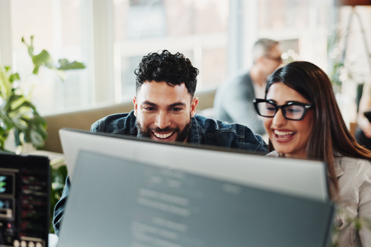 Two colleagues smiling and collaborating in front of a computer screen.