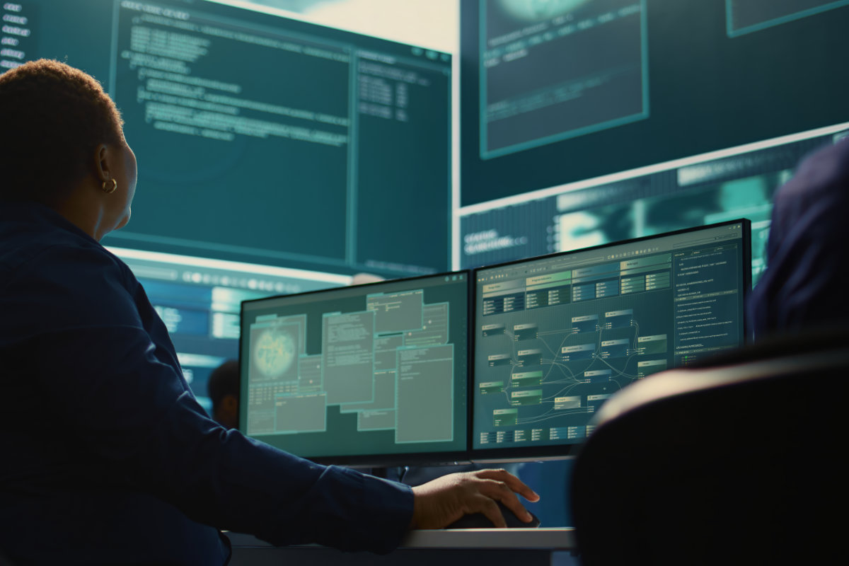 IT professional analyzing system data and code on multiple monitors in a high-tech workspace.