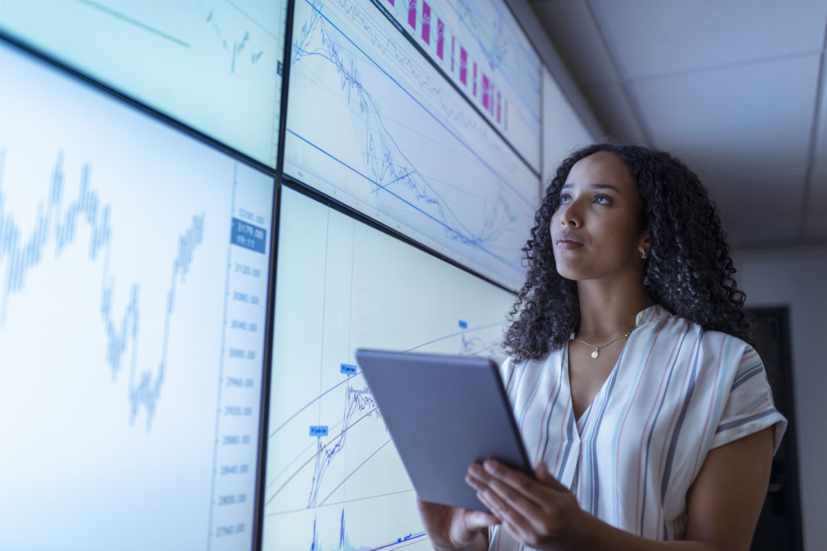 Professional analyzing data on large digital dashboards while holding a tablet, monitoring trends and insights in a modern operations or security environment.